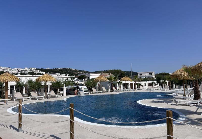 Piscina soleggiata, relax estivo, cielo blu e ombrelloni di paglia.