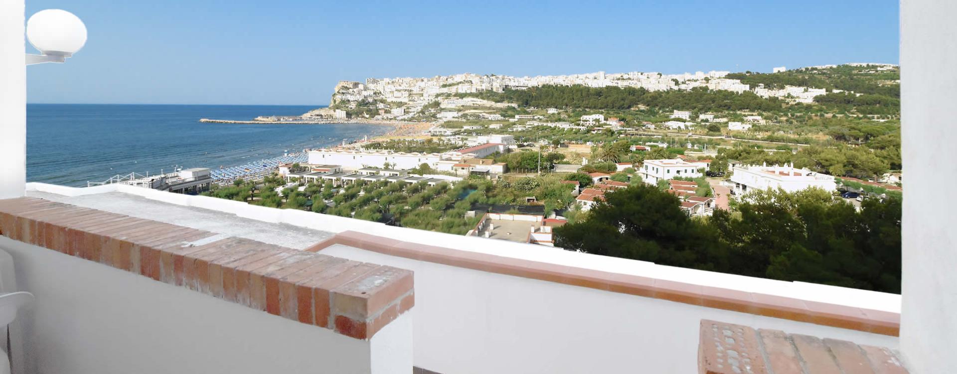 Vista panoramica sul mare con edifici bianchi e colline sullo sfondo.