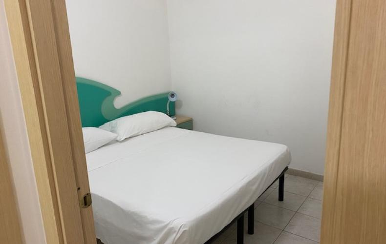 Camera semplice con letto matrimoniale, pareti bianche e testiera verde.