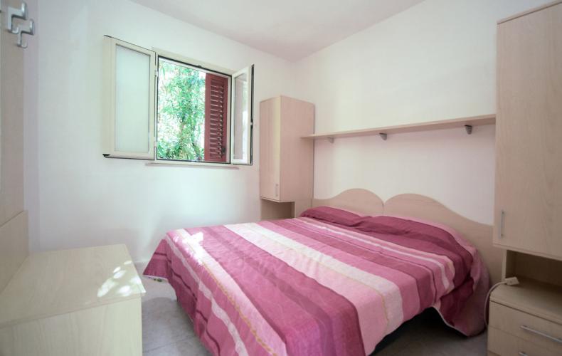 Camera da letto con letto matrimoniale e finestra aperta, arredamento semplice e chiaro.