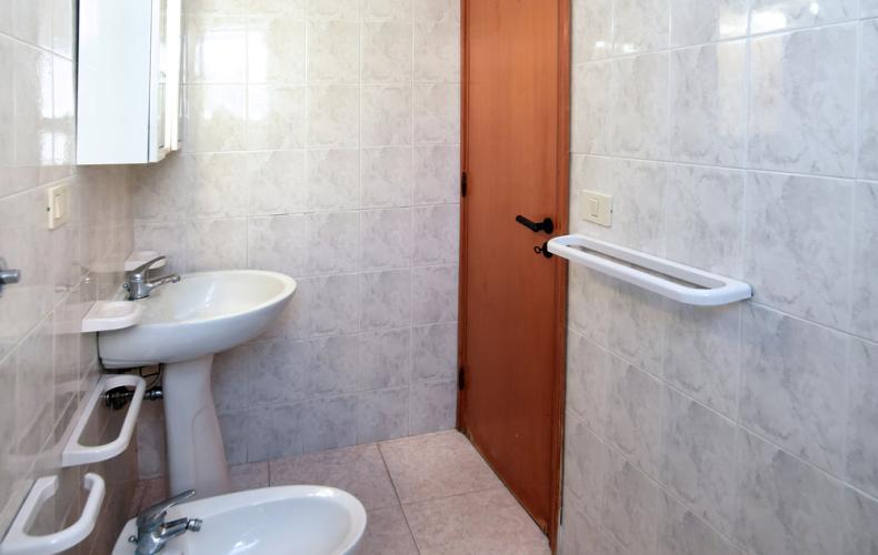 Bagno stretto con sanitari bianchi, piastrelle chiare e porta in legno.