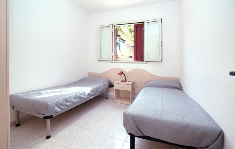 Camera semplice con due letti singoli, finestra e lampada rossa.