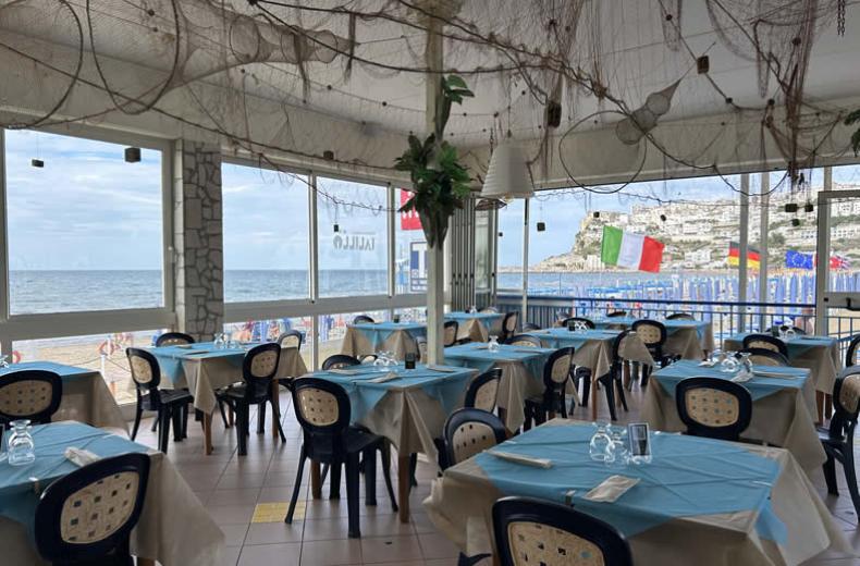 Ristorante sulla spiaggia con tavoli apparecchiati e vista mare.