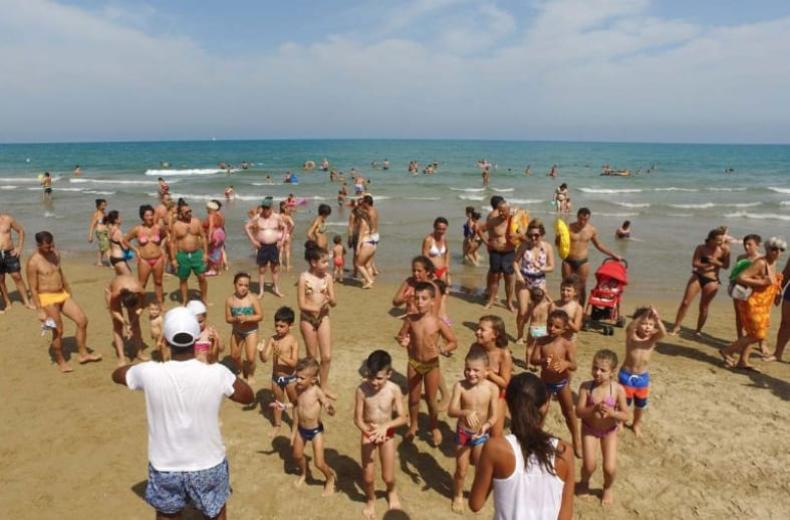 Gruppo di bambini e adulti si divertono sulla spiaggia in una giornata soleggiata.