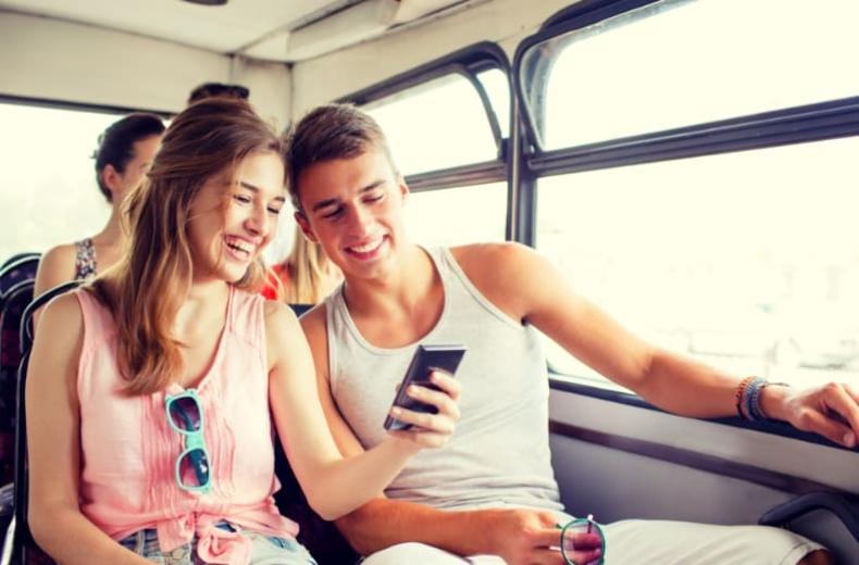 Due amici sorridenti guardano un telefono mentre viaggiano su un autobus.