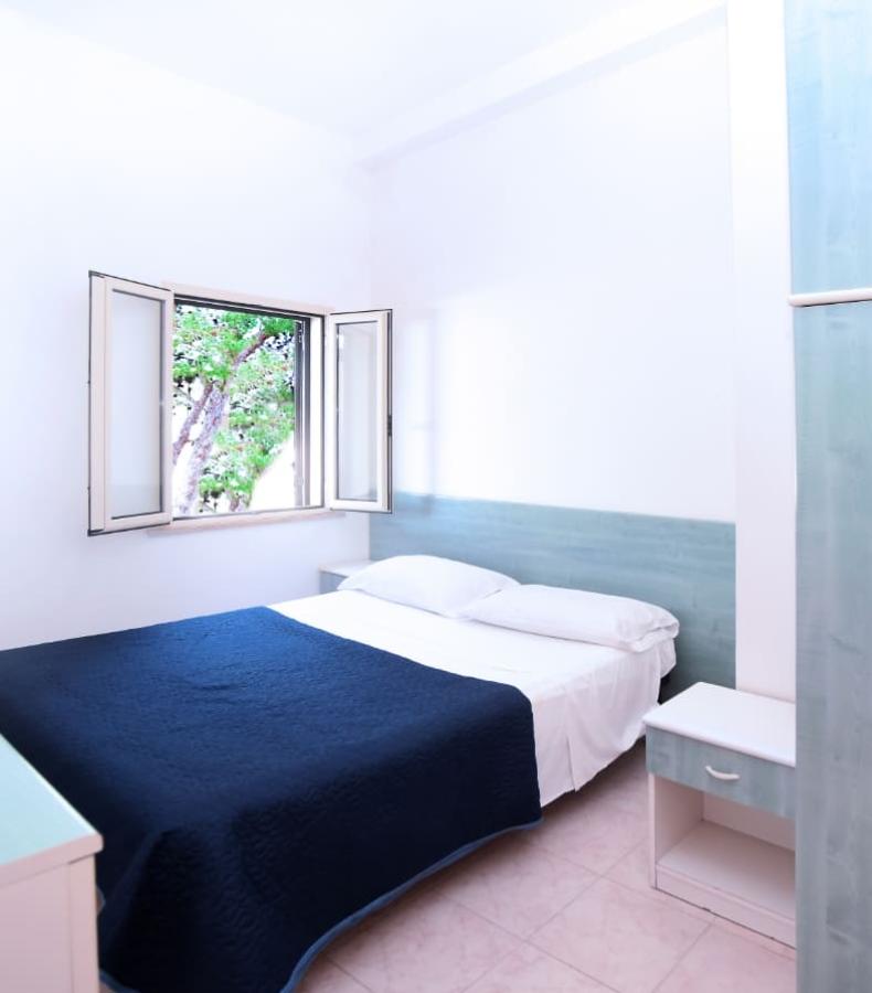 Camera luminosa con letto matrimoniale, coperta blu e finestra aperta con vista alberi.