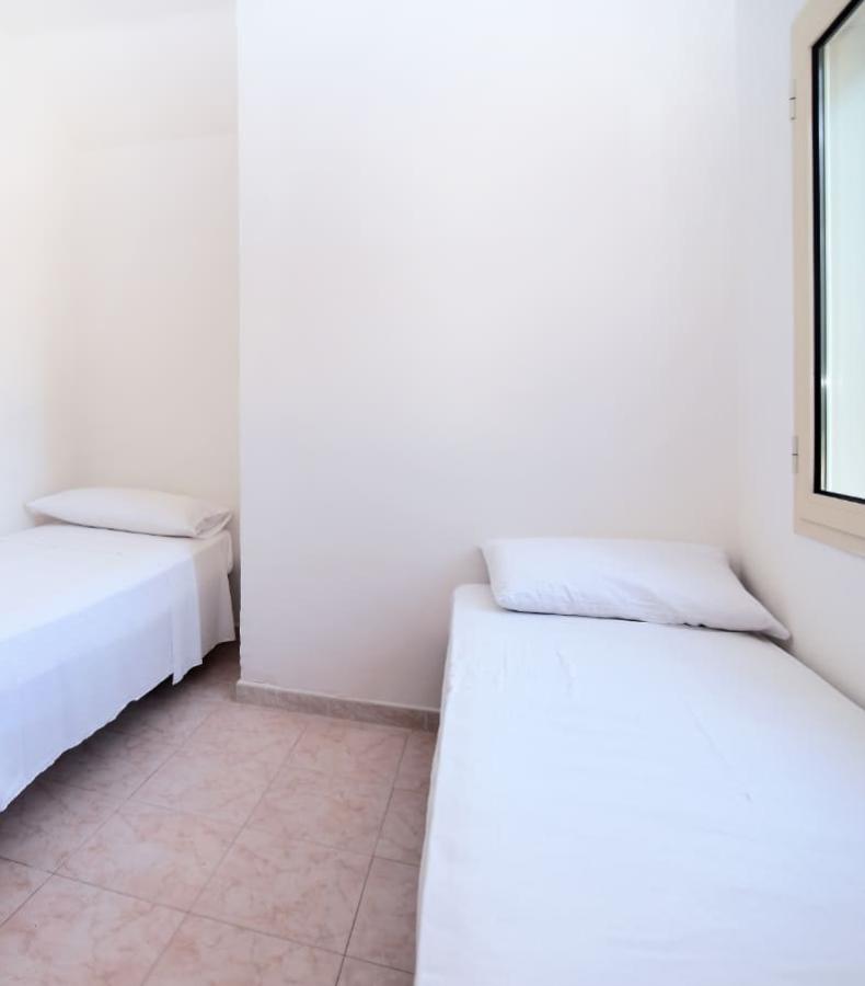 Camera semplice con due letti singoli e finestra, pareti e lenzuola bianche.