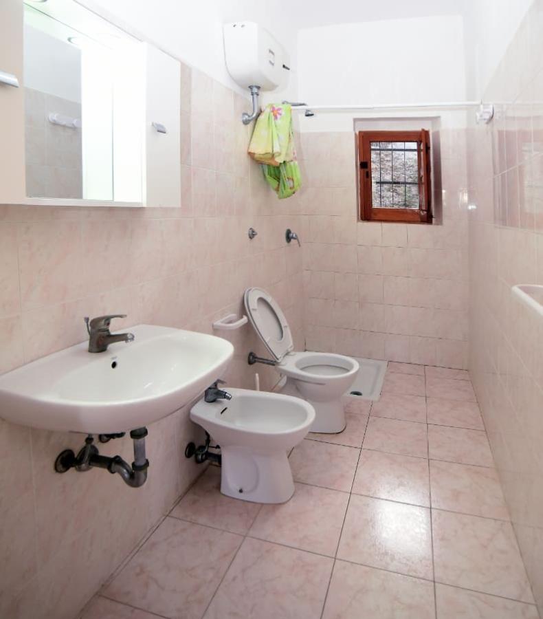 Bagno con lavandino, bidet, WC, doccia e finestra, piastrelle beige.