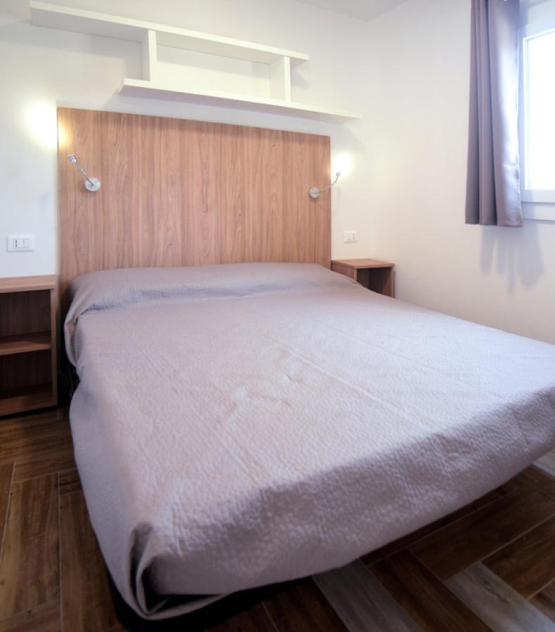 Camera da letto minimalista con letto matrimoniale, testiera in legno e luci da lettura.