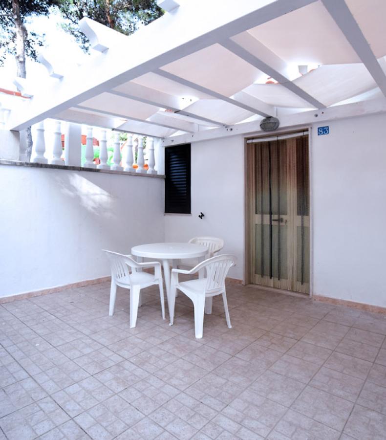 Piccolo patio con tavolo e sedie, coperto da una tettoia bianca.